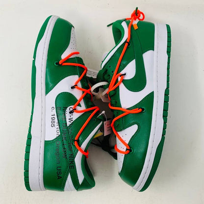 The Nike Dunk Low Off White Pine Green sneaker, accented with bright orange laces, rests on a shiny silver box. This authentic 2019 release by Nike boasts a sleek white tag, highlighting its new allure.