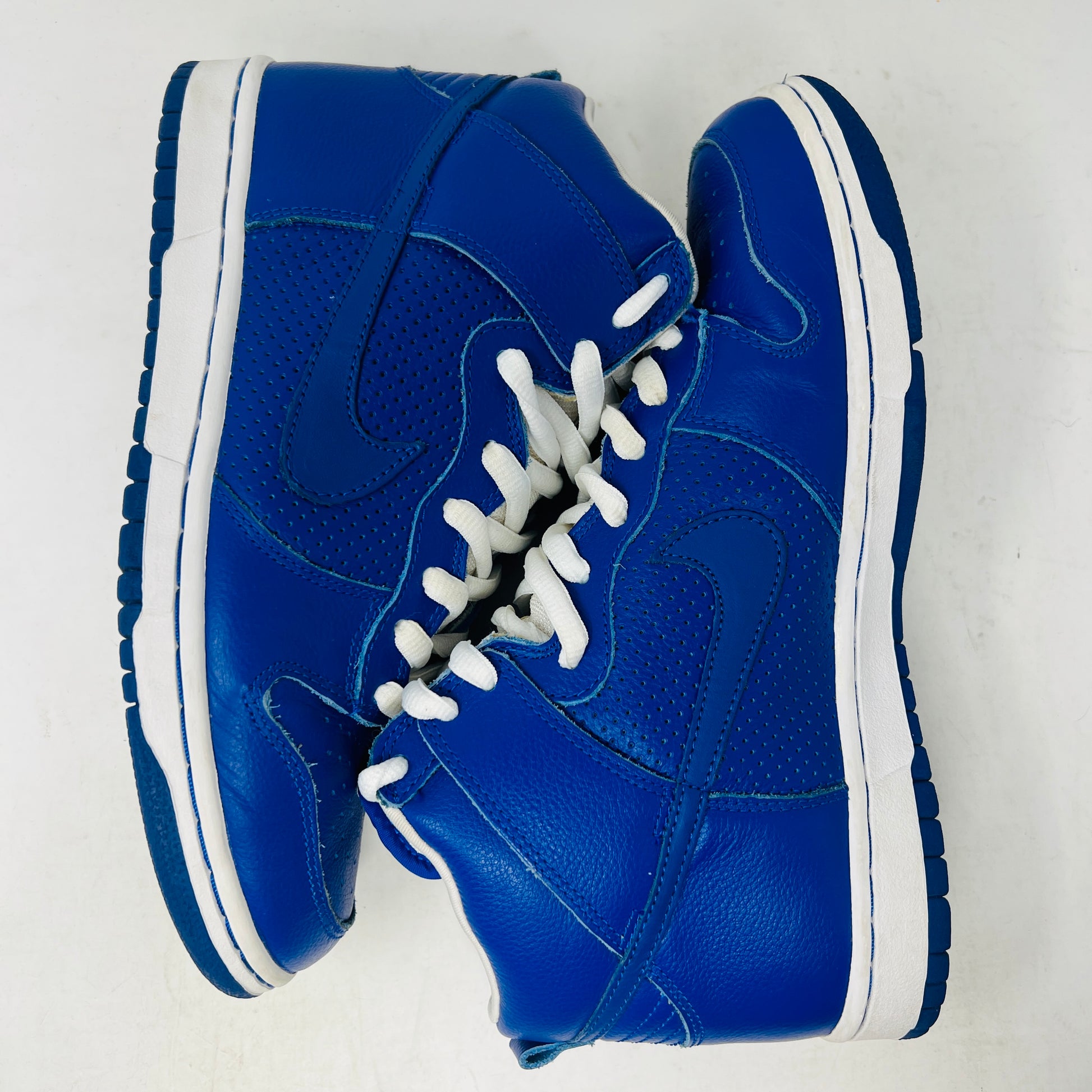 A Nike SB Dunk High T19 Royal Blue sneaker with white laces is perched on a pristine pink shoebox, showcasing the iconic Nike swoosh. The box, in excellent condition, displays a size 10 label.