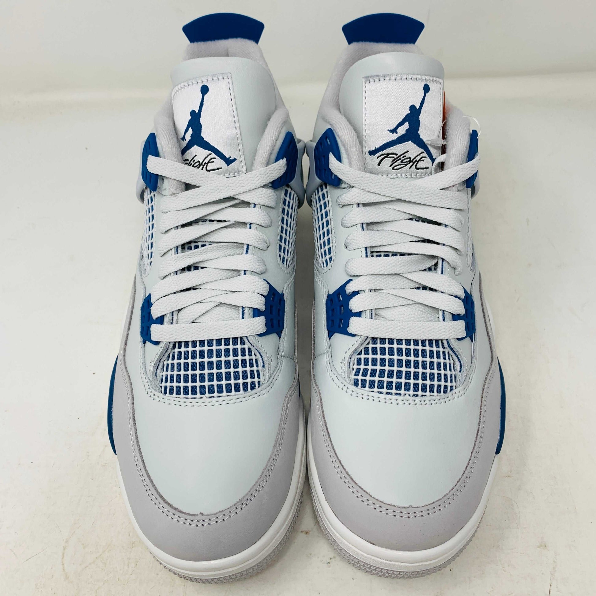 The Jordan 4 Retro Military Blue (2024) sneaker, with white and blue mesh details and a visible air cushion, rests on a black speckled NIKE AIR box with bold orange text. It is 100% authentic, including orange tags, ensuring it’s brand new.