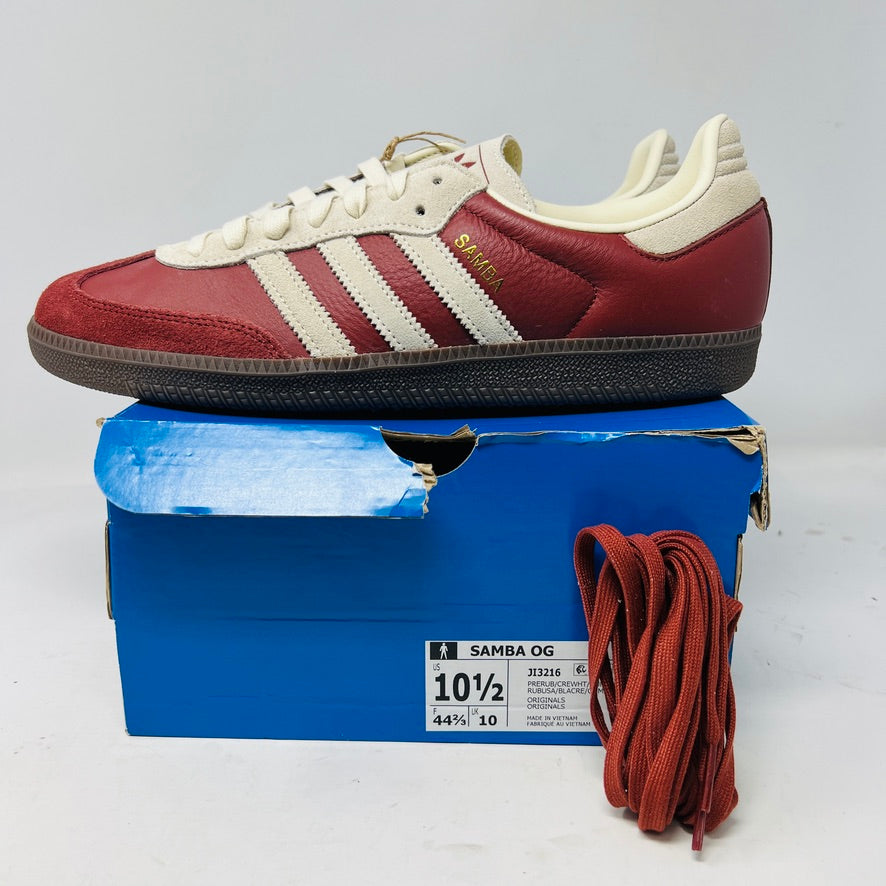 The adidas Samba OG Preloved Ruby Cream White sneaker from Adidas, elegantly displayed on a blue box, comes in size 10½. Featuring white stripes and extra red laces for customization, its ready to step confidently into 2024.
