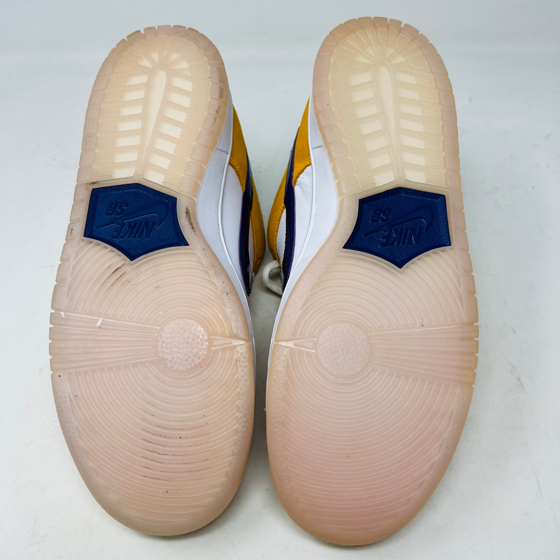 A new Nike SB Dunk Low Laser Orange 8 sneaker, featuring yellow and white suede and leather with a blue swoosh, is displayed on a purple Nike SB box. It includes a white sole, white laces, and extra laces.
