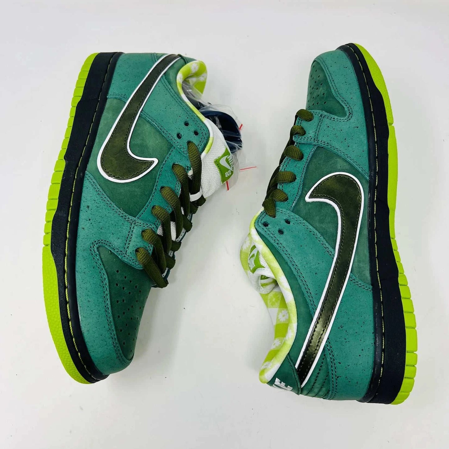 The Nike SB Dunk Low Concepts Green Lobster sneakers, with silver Swooshes and displayed on their Shanghai Special Box, come with extra pink and black laces. They feature green midsoles and a checkered inner lining for that iconic touch.
