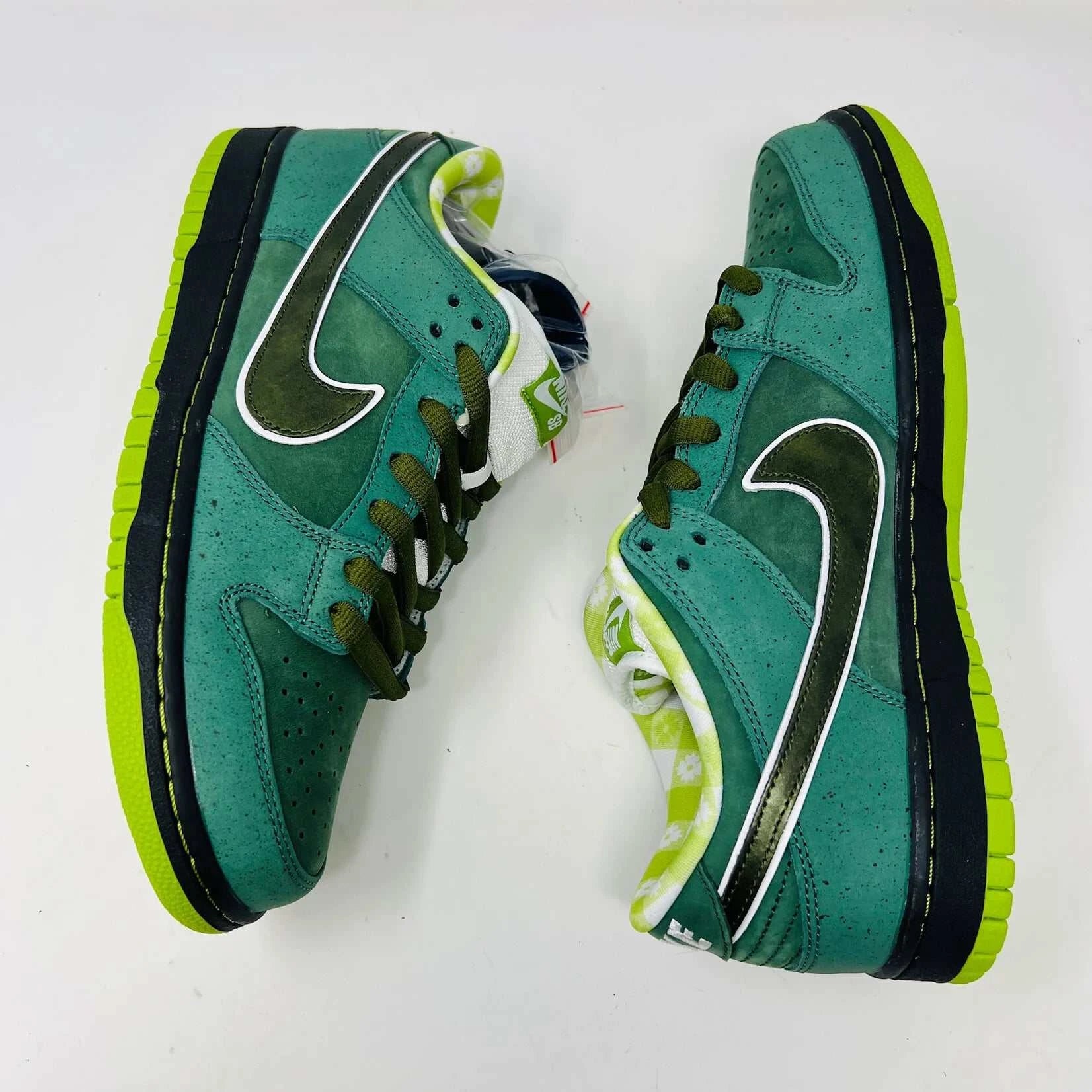 The Nike SB Dunk Low Concepts Green Lobster sneakers, with silver Swooshes and displayed on their Shanghai Special Box, come with extra pink and black laces. They feature green midsoles and a checkered inner lining for that iconic touch.