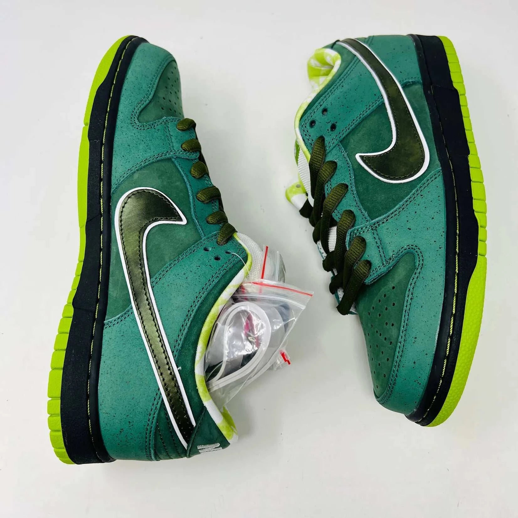 The Nike SB Dunk Low Concepts Green Lobster sneakers, with silver Swooshes and displayed on their Shanghai Special Box, come with extra pink and black laces. They feature green midsoles and a checkered inner lining for that iconic touch.