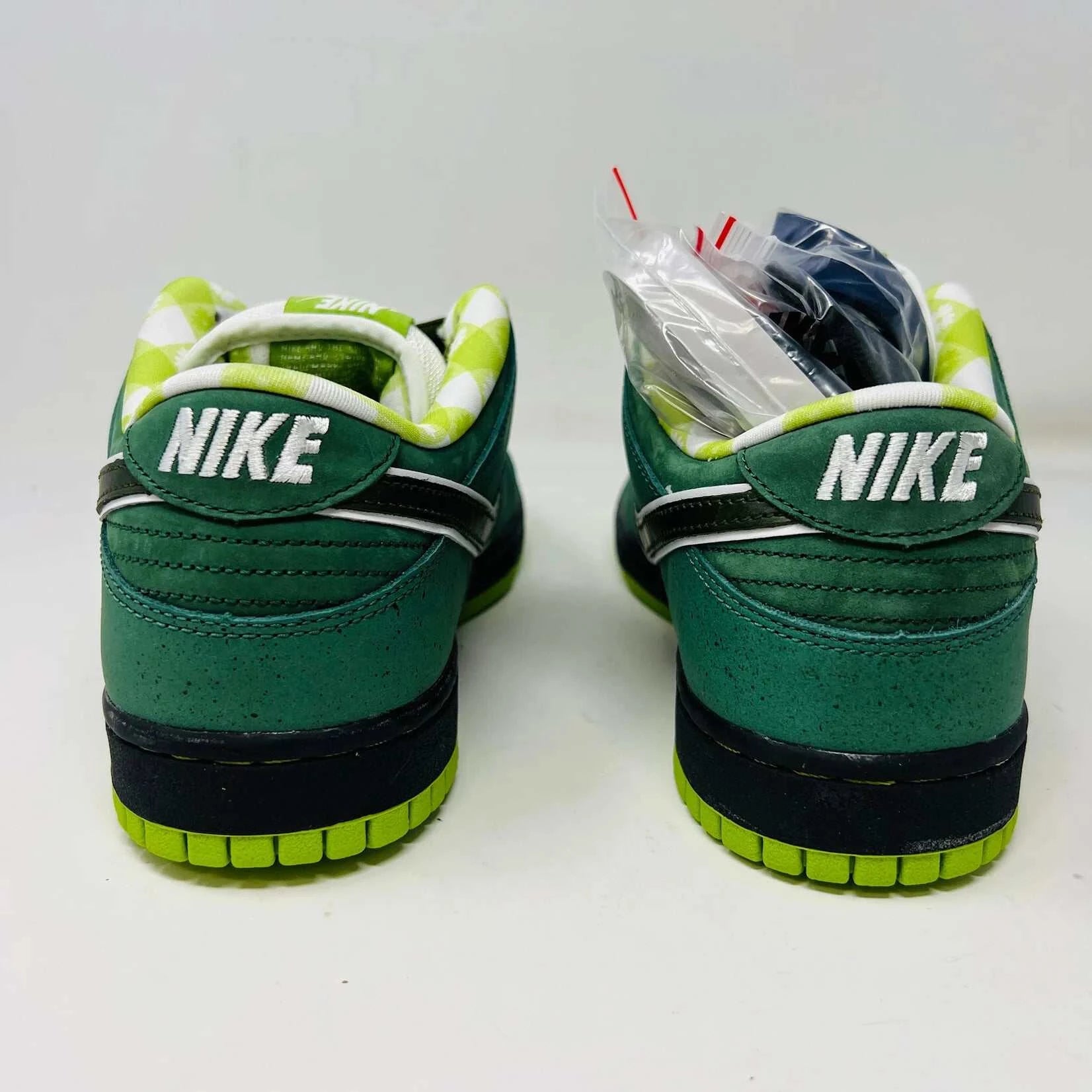 The Nike SB Dunk Low Concepts Green Lobster sneakers, with silver Swooshes and displayed on their Shanghai Special Box, come with extra pink and black laces. They feature green midsoles and a checkered inner lining for that iconic touch.