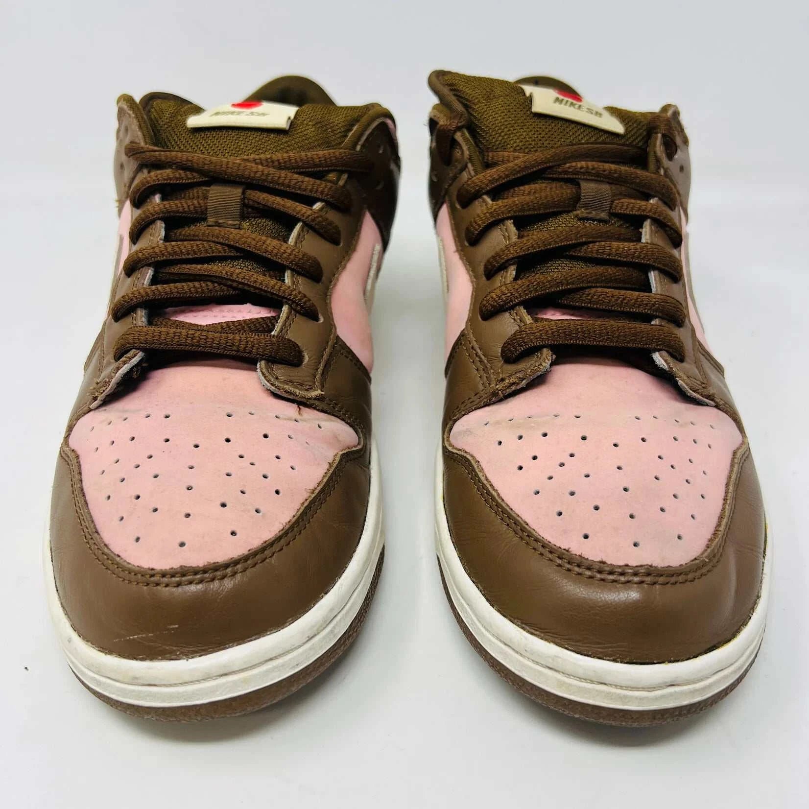 The Nike SB Dunk Low Stussy Cherry sneakers, in brown and pink with white midsoles, feature brown laces and a brand tag on the tongue, set against a plain white background.