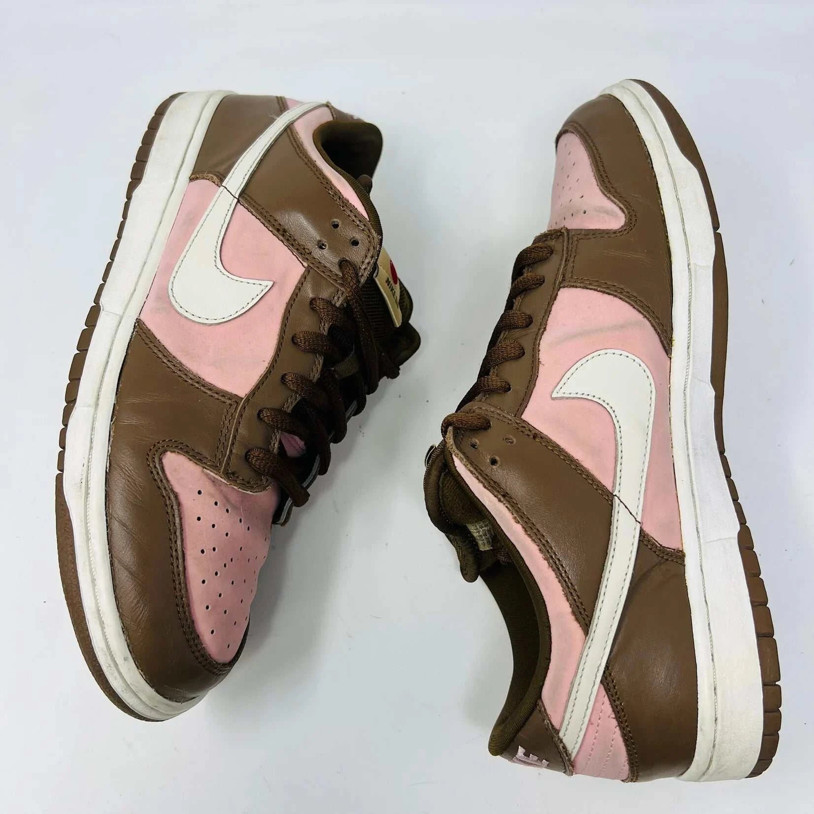 The Nike SB Dunk Low Stussy Cherry sneakers, in brown and pink with white midsoles, feature brown laces and a brand tag on the tongue, set against a plain white background.