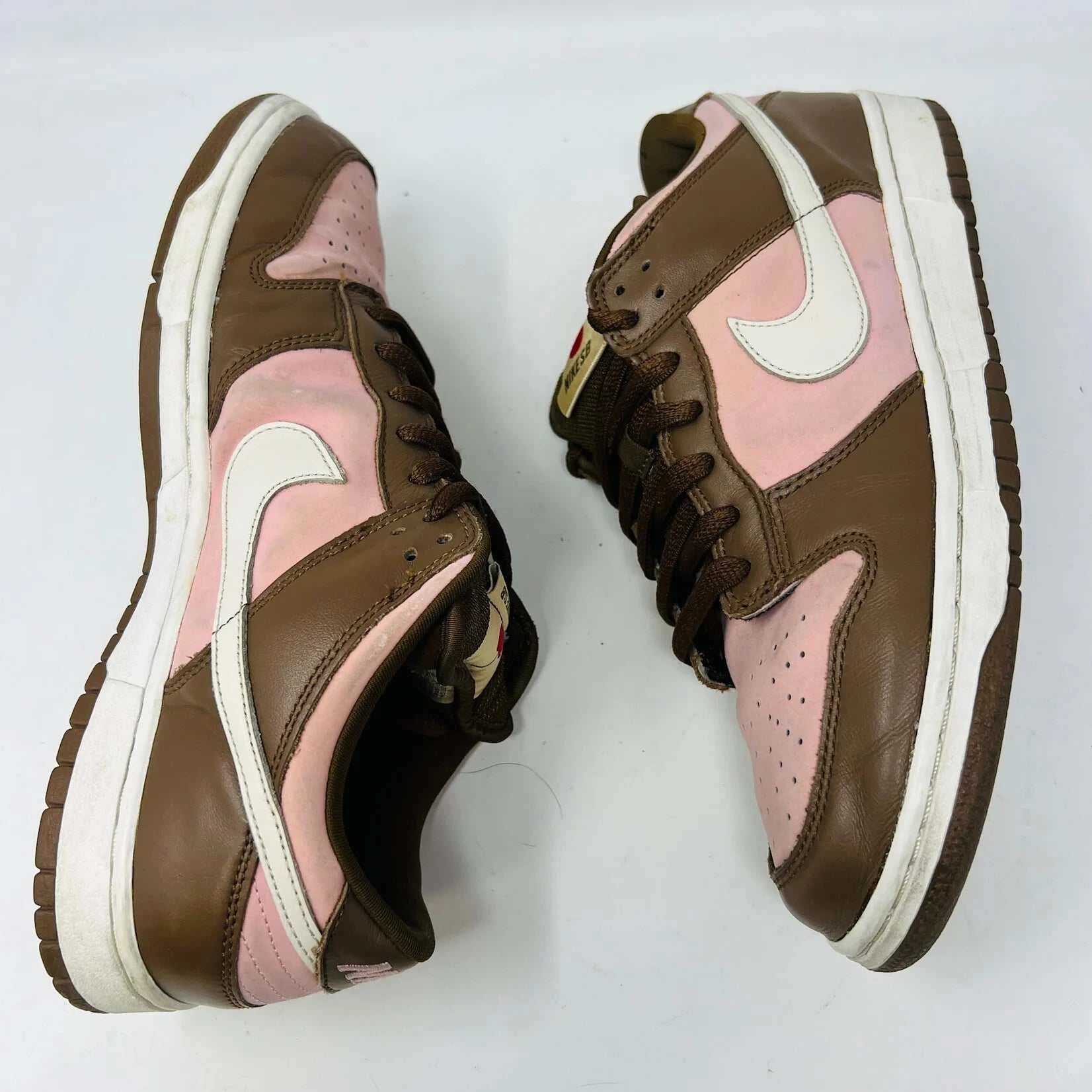 The Nike SB Dunk Low Stussy Cherry sneakers, in brown and pink with white midsoles, feature brown laces and a brand tag on the tongue, set against a plain white background.