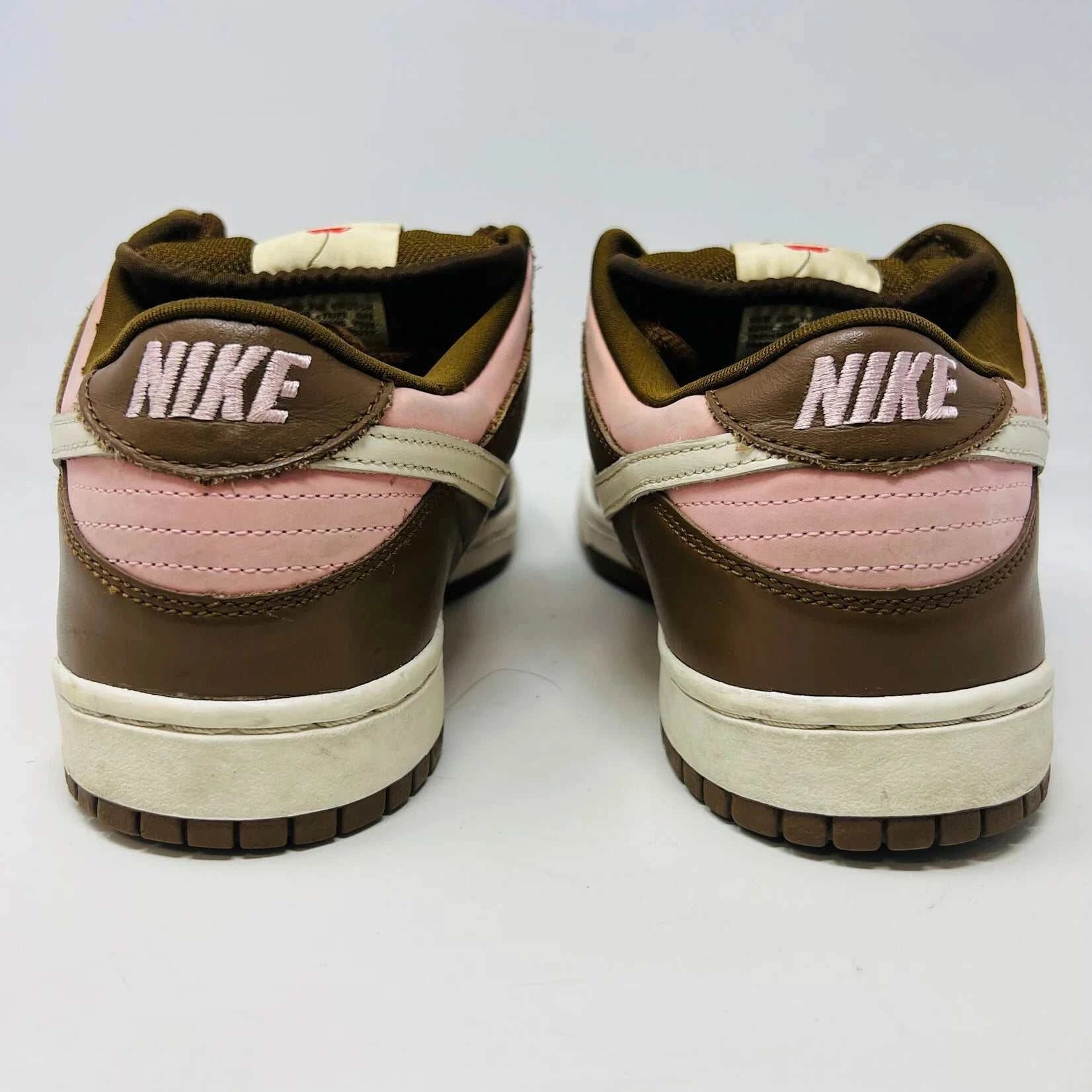 The Nike SB Dunk Low Stussy Cherry sneakers, in brown and pink with white midsoles, feature brown laces and a brand tag on the tongue, set against a plain white background.