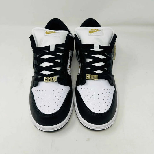 The authentic Nike SB Dunk Low Supreme Stars Black (2021) sneaker, featuring a gold star pattern and a WORLD FAMOUS Supreme tag, is presented in a purple Nike SB box with extra laces.
