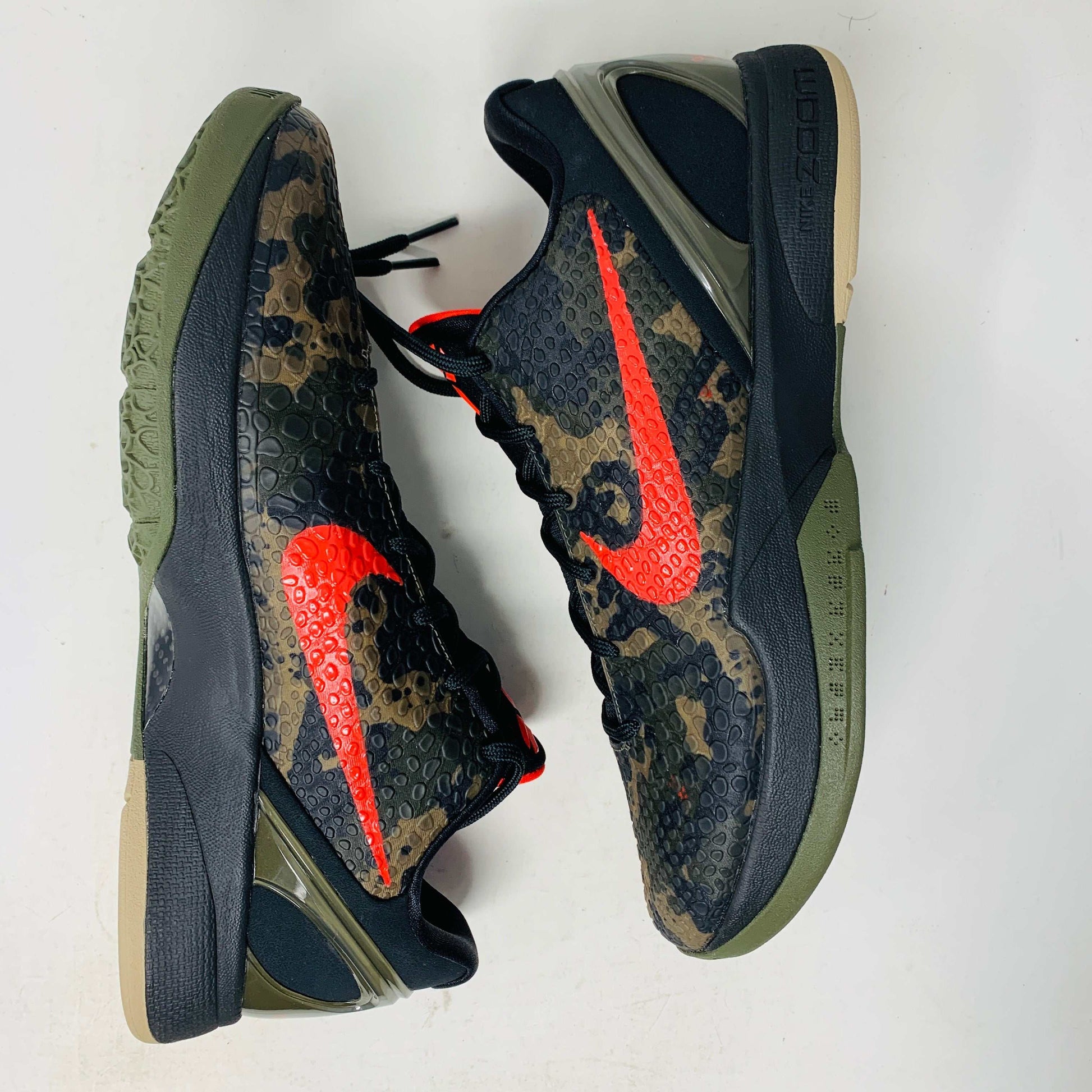 The 2024 Nike Kobe 6 Protro Italian Camo features a textured gray upper with a bright red swoosh, sits on a black shoe box, and has a greenish midsole labeled Zoom. The sleek black lace system completes this authentic sporty sneaker.
