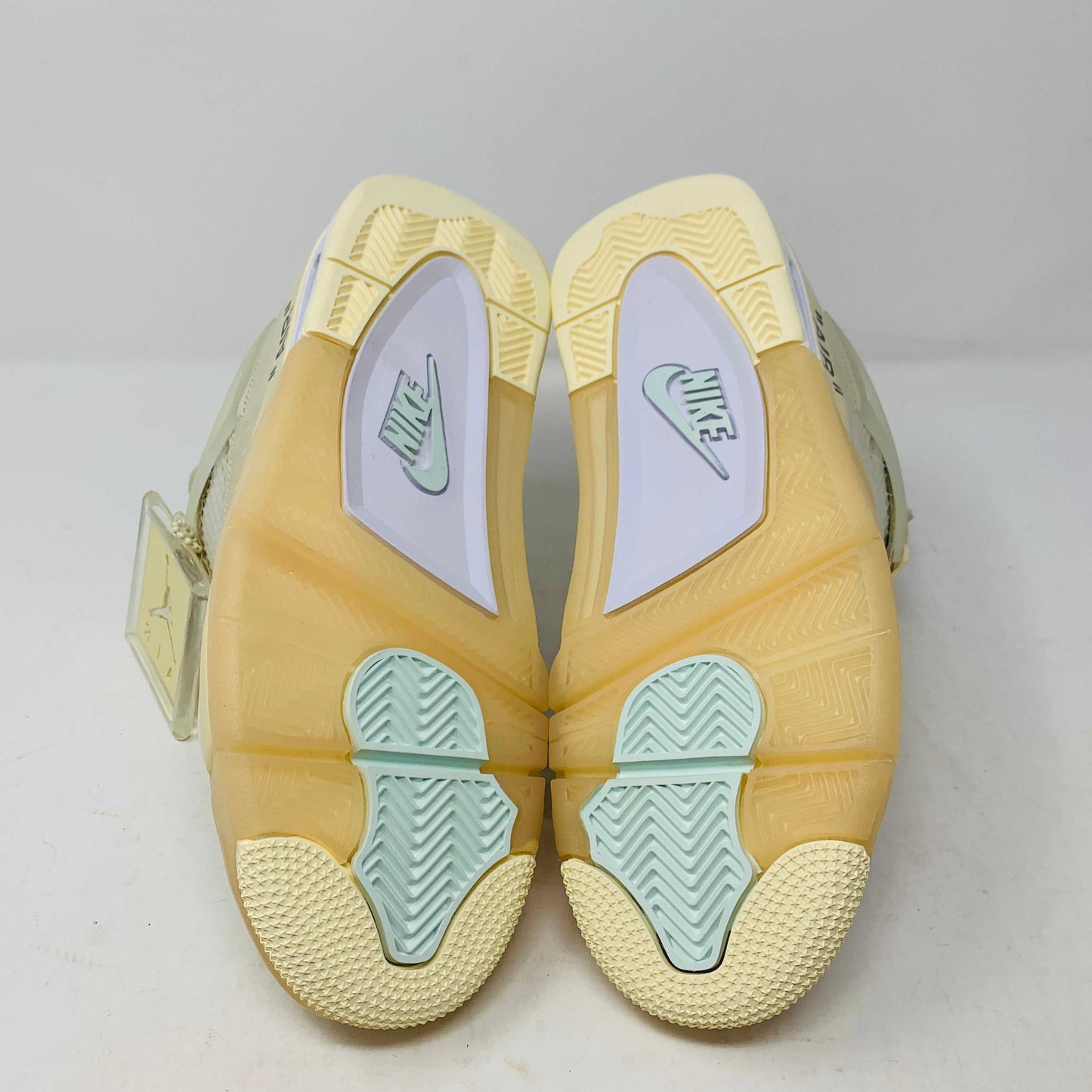 A beige Jordan 4 Off White Sail W sneaker rests on a box with the authentic Air Jordan logo. It comes with three extra sets of laces in mint, cream, and black labeled SHOELACES, a plastic zip tie, and features a small Jumpman Air tag.