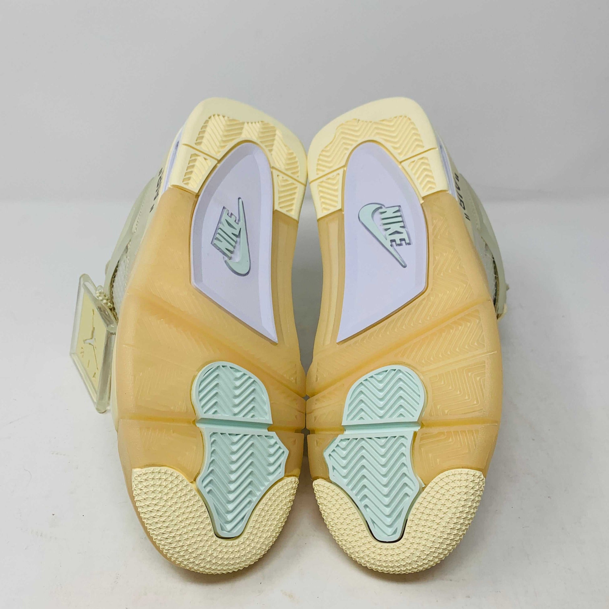 A beige Jordan 4 Off White Sail W sneaker rests on a box with the authentic Air Jordan logo. It comes with three extra sets of laces in mint, cream, and black labeled SHOELACES, a plastic zip tie, and features a small Jumpman Air tag.