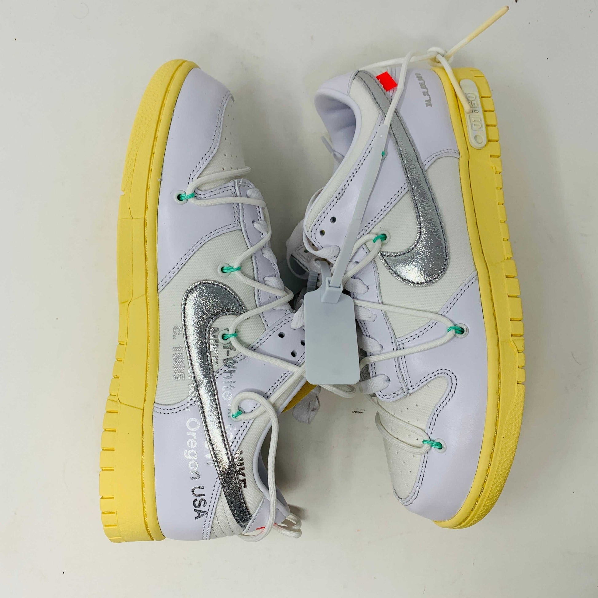 The Nike Dunk Low Off White Lot 1 sneaker, white with a metallic silver swoosh and vibrant accents, rests on a brown shoebox. Its unique lace design and 01 of 50 detailing highlight its 2021 release against a plain white backdrop.