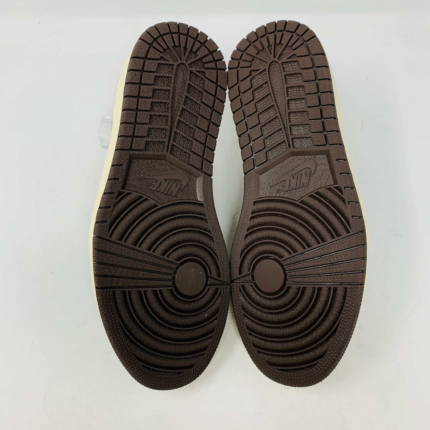 A pair of BRAND NEW Jordan 1 Low OG Travis Scott Mocha sneakers in black and brown, featuring a white swoosh, displayed on a brown shoe box with a red logo. 100% Authentic with EXTRA LACES partially visible inside.