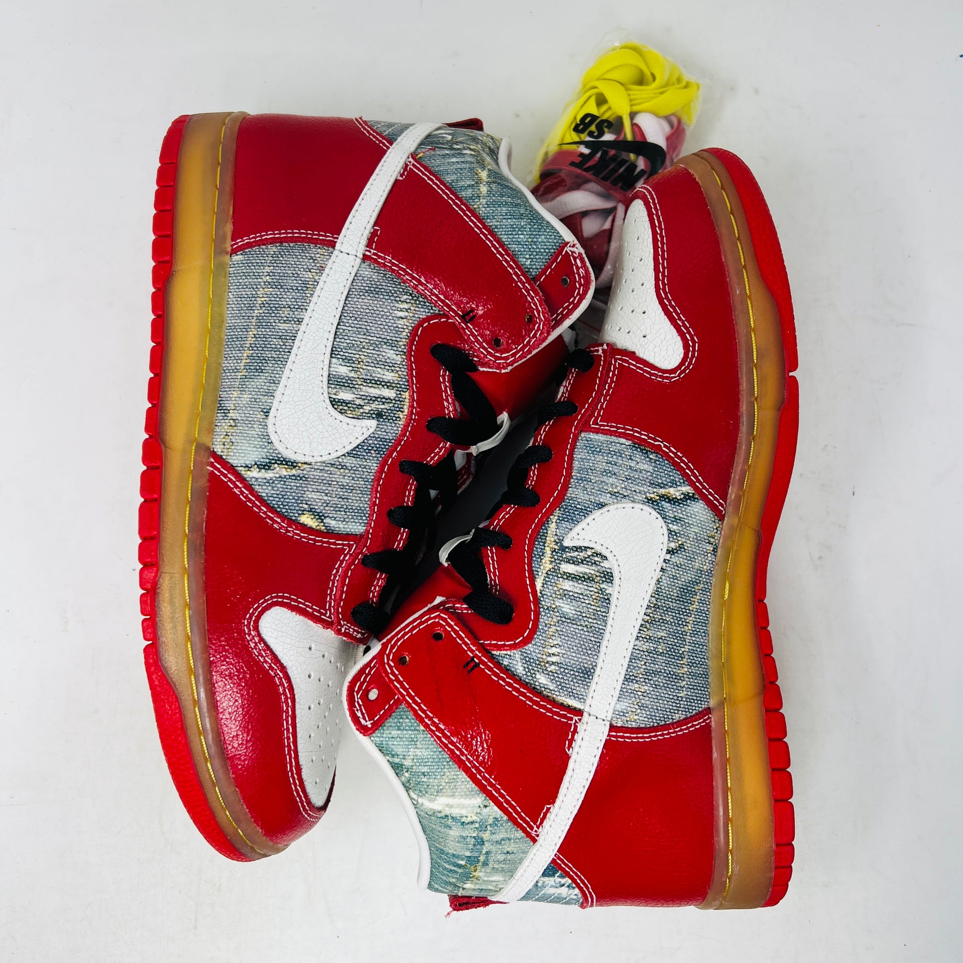 The Nike SB Dunk High Shoe Goo from 2008, priced at $525, sits atop its box. It features red and blue denim sections, a white swoosh, and a gum sole. A tag shows size and numbers, with extra laces beside the shoebox.