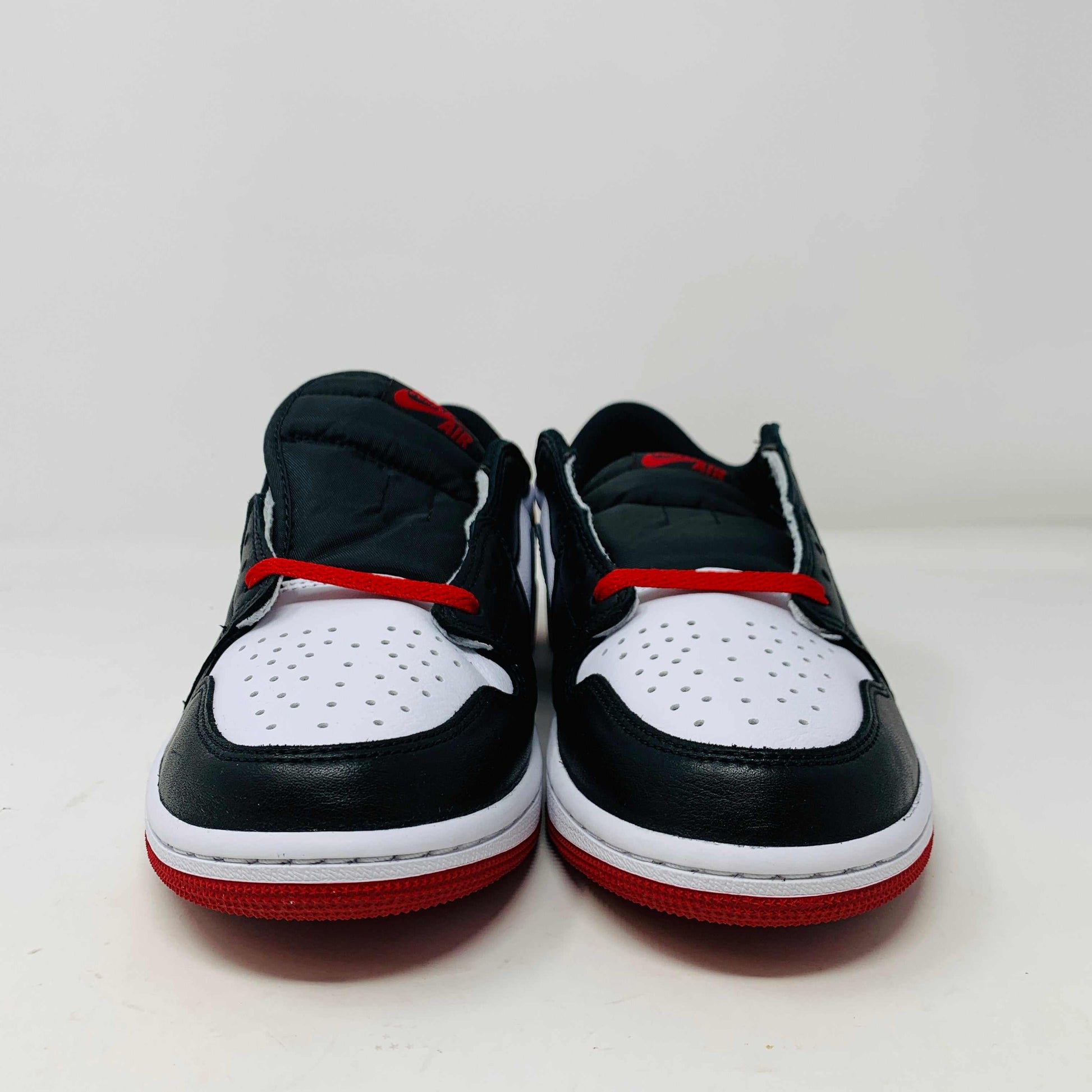 Discover the Jordan 1 Retro Low OG Black Toe (2023) sneakers featuring genuine black and white leather panels, red laces, and soles. These low-tops from Jordan come with extra laces and are displayed on a clean white surface against a pristine background.
