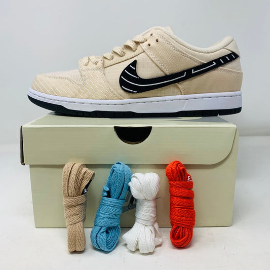 The Nike SB Dunk Low Albino and Preto rests on a shoebox, embodying skateboarding sneaker essence, with a beige finish, black swoosh, black sole, white midsole, and premium leather laces in beige, blue, white, and red.
