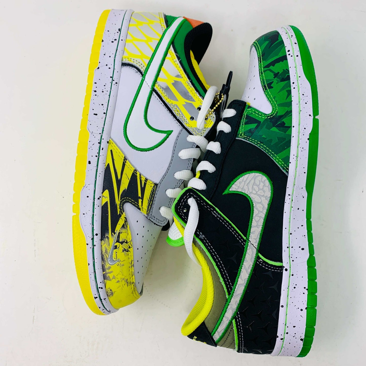 The Nike Dunk Low What the Duck Away University of Oregon PE is a vibrant sneaker featuring green, white, and black patterns with a black Nike swoosh outlined in yellow. It includes white laces, extra laces, a speckled white midsole, and a padded yellow lining atop a bright green shoebox. 100% authentic.