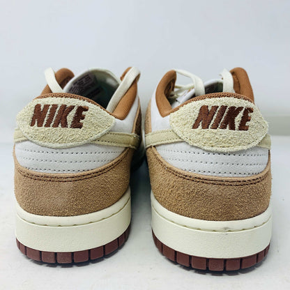 A brand new pair of Nike Dunk Low Medium Curry sneakers, with a beige suede upper and white swoosh accents, rests in pristine condition on a red box featuring the bold white Nike logo, set against a plain backdrop.