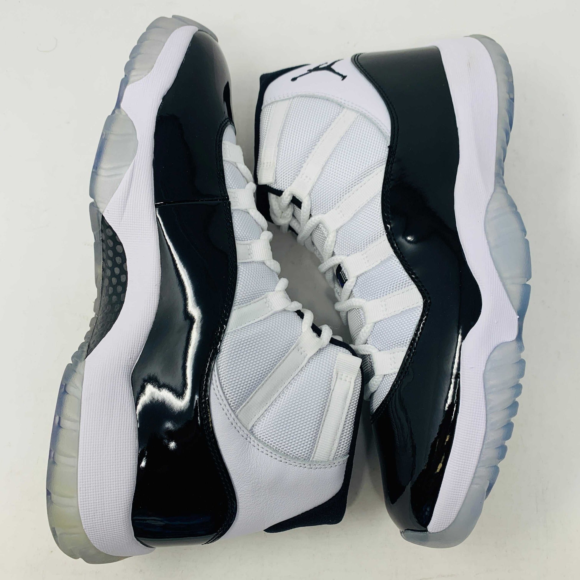 A BRAND NEW black and white Jordan 11 Concord 2018 sneaker sits on its shoebox, showcasing a glossy black patent leather finish and white mesh upper with the iconic Jumpman logo. The shoebox, bearing a white Nike Air logo, ensures these shoes are 100% authentic.