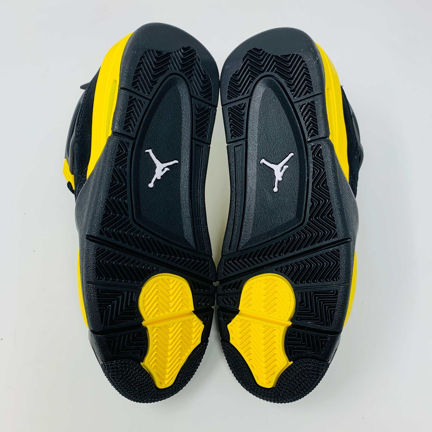 Brand new for 2023, the Jordan 4 Retro Thunder (GS) sneakers in black and yellow feature mesh panels and air cushioning. Positioned on a white background, they showcase their unique color scheme and design.