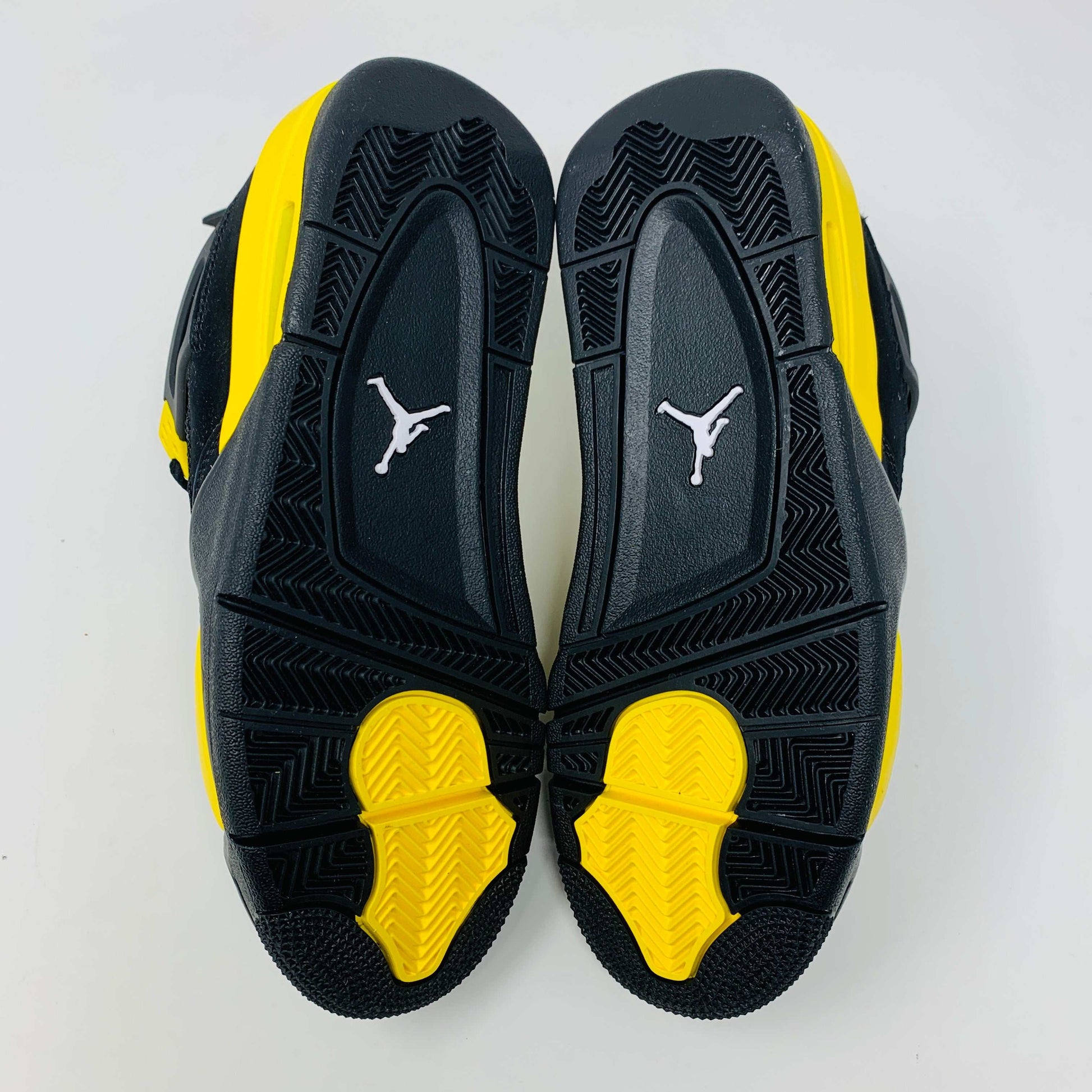 Brand new for 2023, the Jordan 4 Retro Thunder (GS) sneakers in black and yellow feature mesh panels and air cushioning. Positioned on a white background, they showcase their unique color scheme and design.
