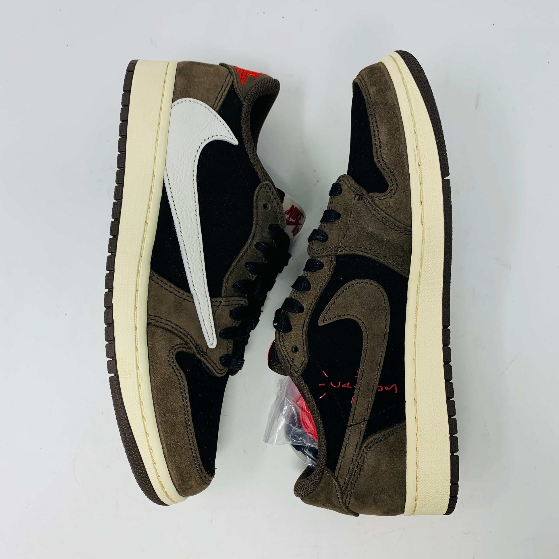 A pair of BRAND NEW Jordan 1 Low OG Travis Scott Mocha sneakers in black and brown, featuring a white swoosh, displayed on a brown shoe box with a red logo. 100% Authentic with EXTRA LACES partially visible inside.