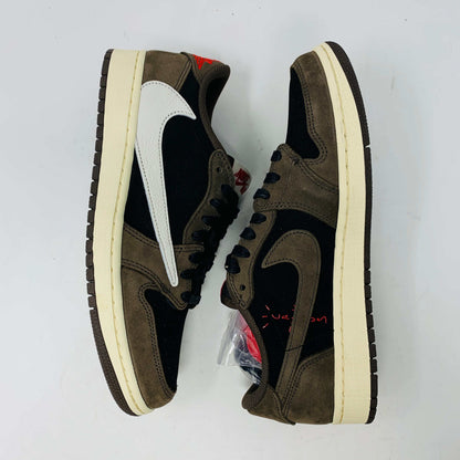 A pair of BRAND NEW Jordan 1 Low OG Travis Scott Mocha sneakers in black and brown, featuring a white swoosh, displayed on a brown shoe box with a red logo. 100% Authentic with EXTRA LACES partially visible inside.