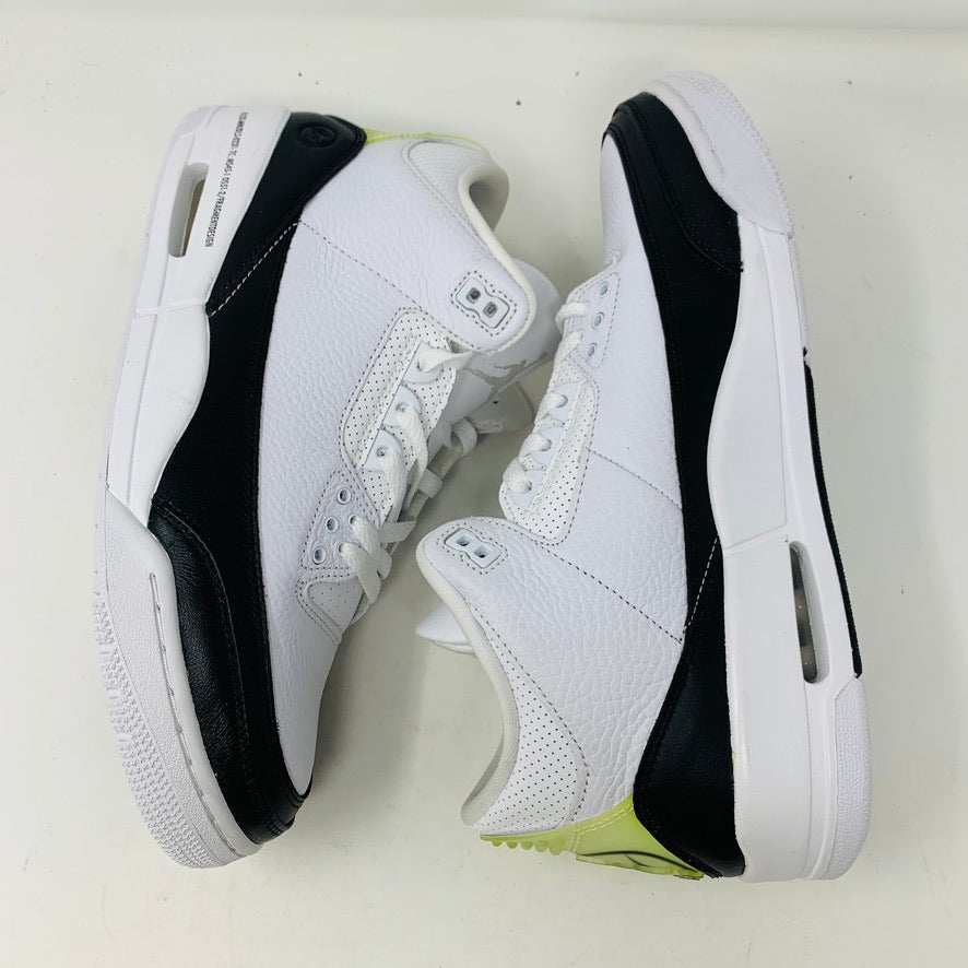 The Jordan 3 Fragment by Jordan, a white sneaker with black midsole and lime green heel detailing, is displayed on a closed blue shoebox.