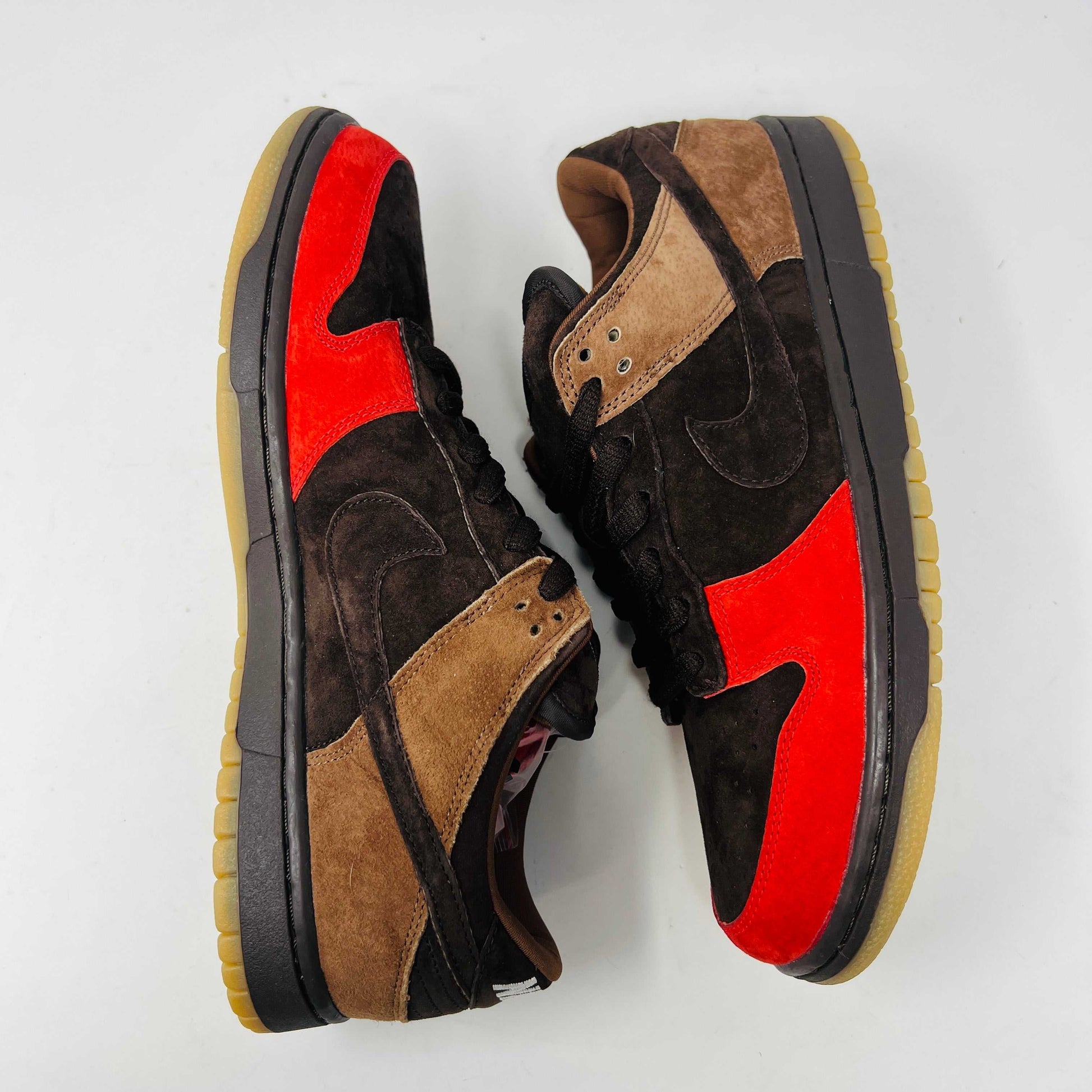 A pair of BRAND NEW Nike SB Dunk Low Bison sneakers featuring brown and red suede uppers, black laces, EXTRA LACES included, and a light brown sole. Positioned side by side on a white background, they promise to be 100% authentic and stylish.