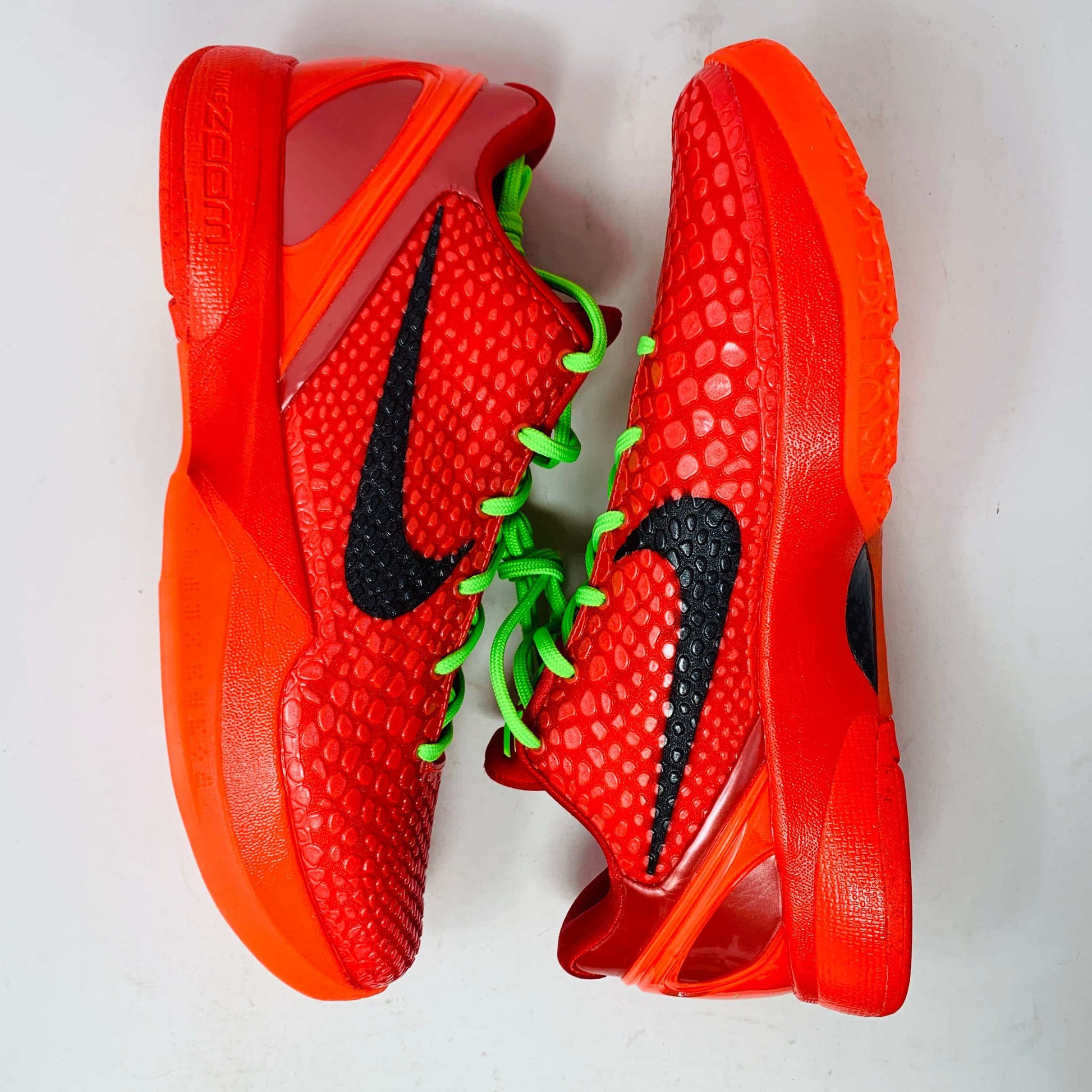 The Nike Kobe 6 Protro Reverse Grinch features a vibrant red colorway with black swoosh logos and bright green laces. Displayed on a white background, these athletic basketball shoes have soles and heel areas matching the bold red hue.