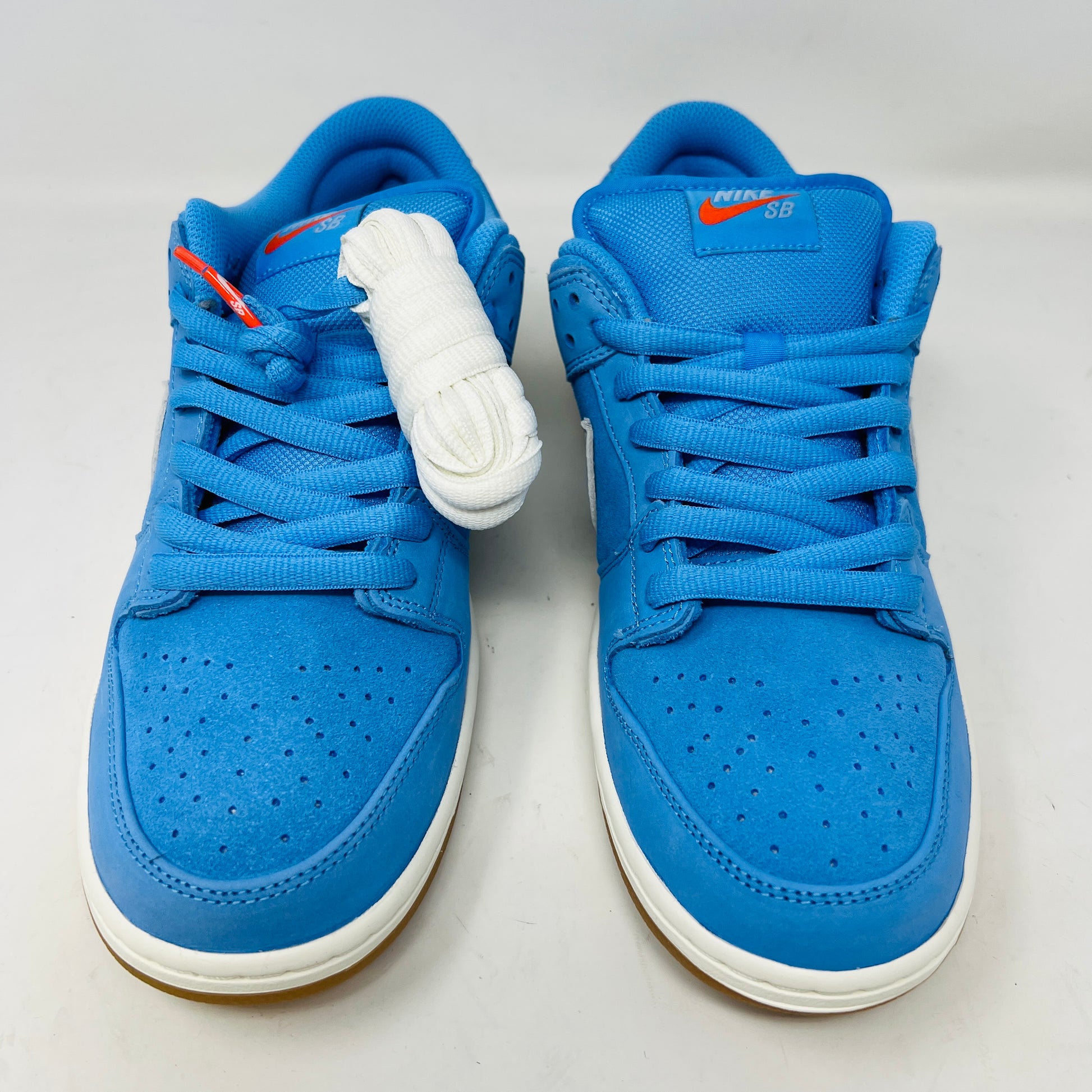 The Nike SB Dunk Low Pro University Blue Gum sneaker, featuring a white swoosh, laces, midsole, and gum-colored outsole, is placed on a brown shoebox with an orange swoosh against a plain white background.