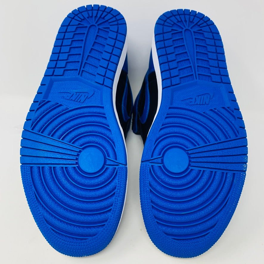 A pair of brand new black and blue Jordan 1 Royal 2017 high-tops are showcased on a black and red Nike box, with a small plastic bag holding authentic blue laces attached to one shoe.