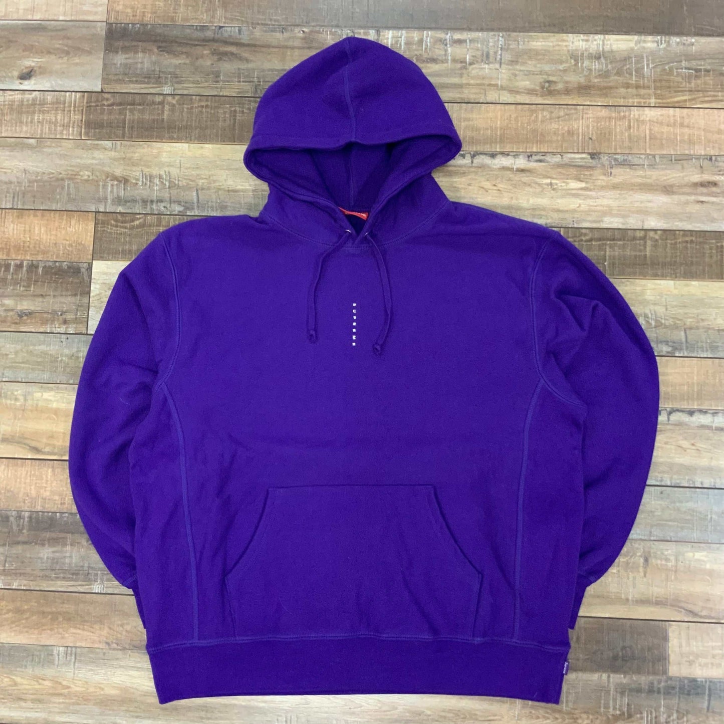 Purple Supreme Micro Logo Hooded Sweatshirt with small front branding, laid flat on wooden floor