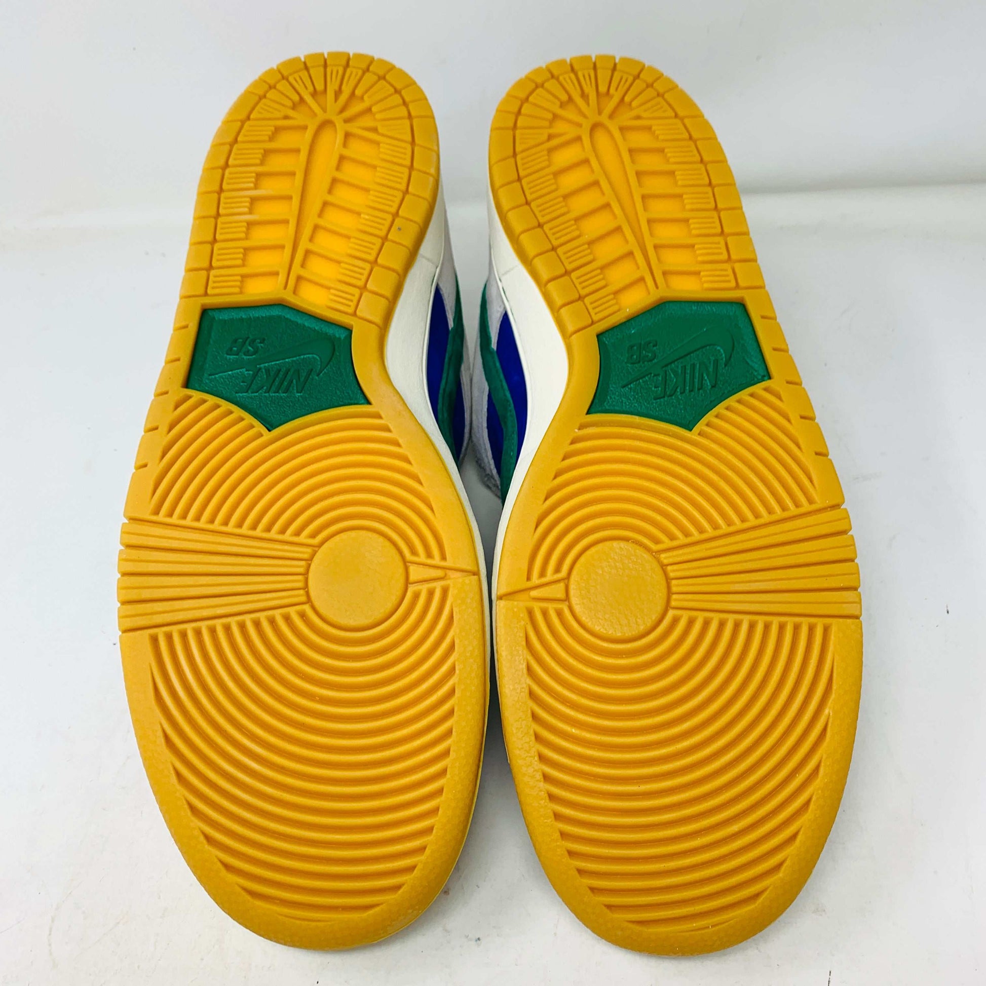 The Nike SB Dunk Low Hyper Royal Malachite, a fresh pair of white and blue sneakers with a green swoosh and gum sole, includes extra laces and is presented atop a purple Nike SB shoe box.