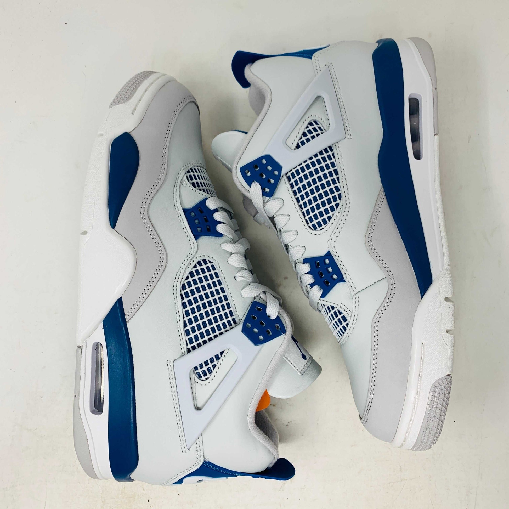 The Jordan 4 Retro Military Blue (2024) sneaker, with white and blue mesh details and a visible air cushion, rests on a black speckled NIKE AIR box with bold orange text. It is 100% authentic, including orange tags, ensuring it’s brand new.