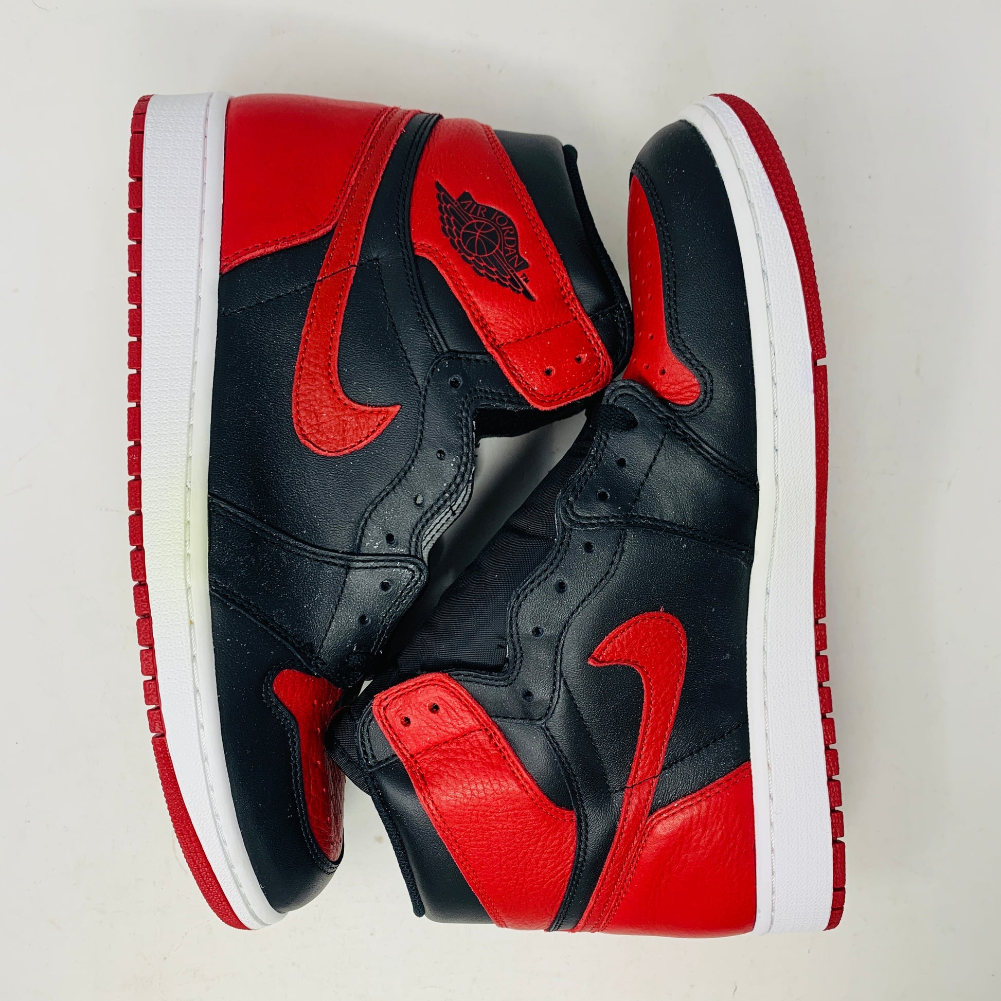 The Jordan 1 High Bred 2016 sneakers, by Jordan, are brand-new black and red high-tops with a white sole. Viewed from above, they showcase an unlaced look with a perforated design on the toe area.