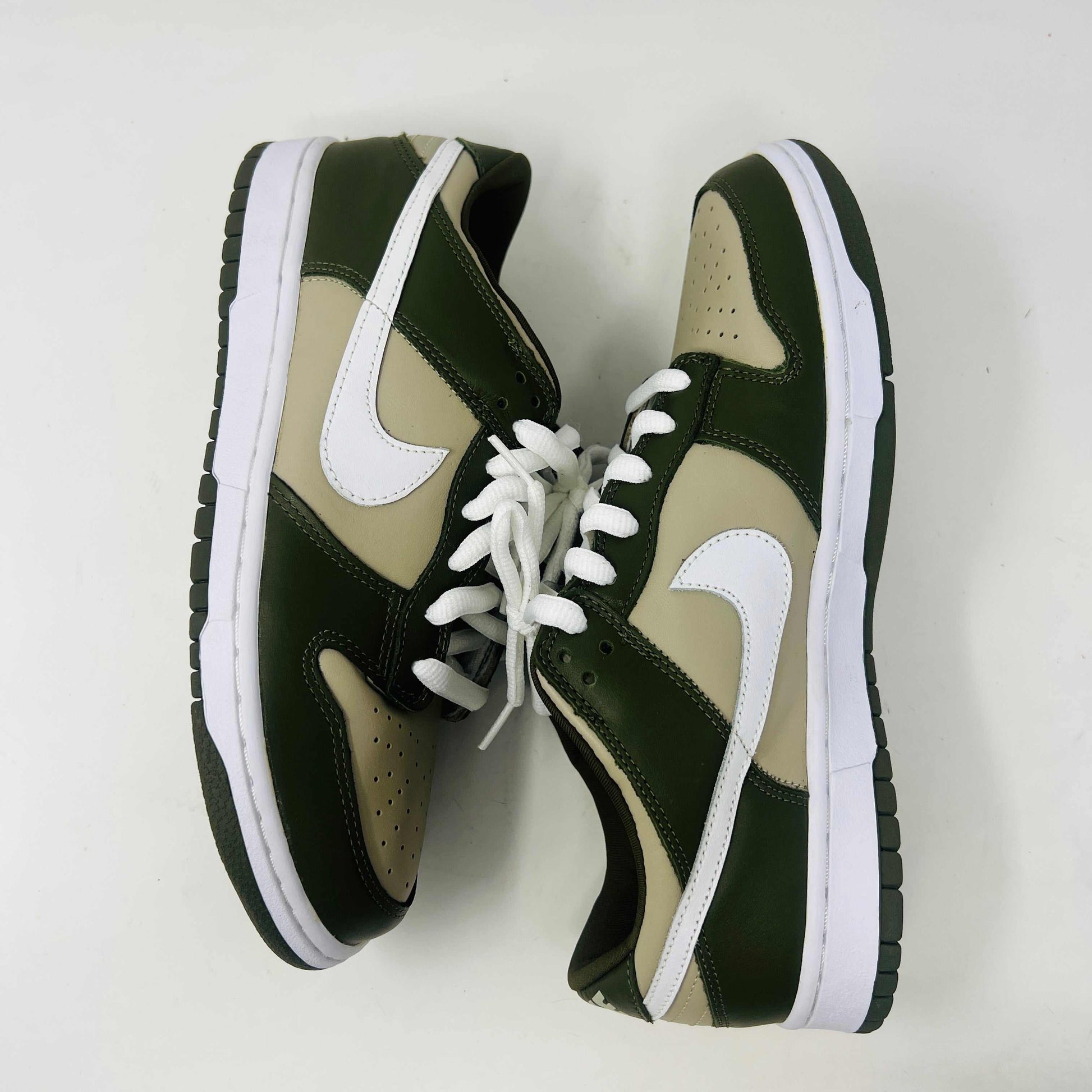 A Nike Dunk Low Light Stone shoe in green and beige with brand new white laces is displayed atop an orange Nike box. Extra white laces are in front, ensuring this 100% authentic pair from the Nike Dunk collection is ready to step out in style.