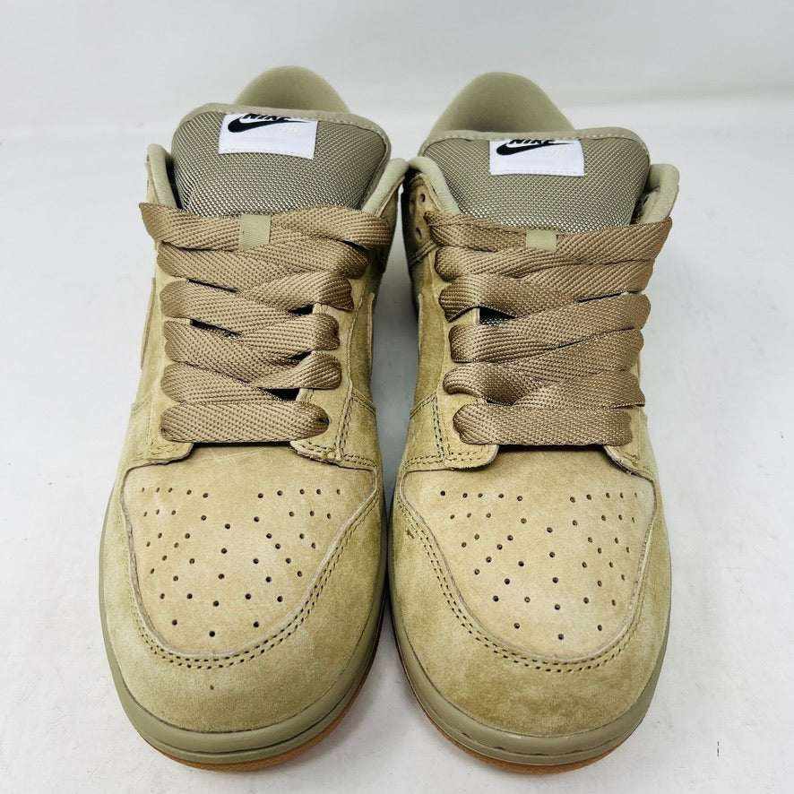 The Nike SB Dunk Low Pro B Parachute Beige, with a beige swoosh and gum sole, is displayed on a purple Nike SB box. New tan suede sneaker includes extra laces neatly rolled up in front against a plain white background.