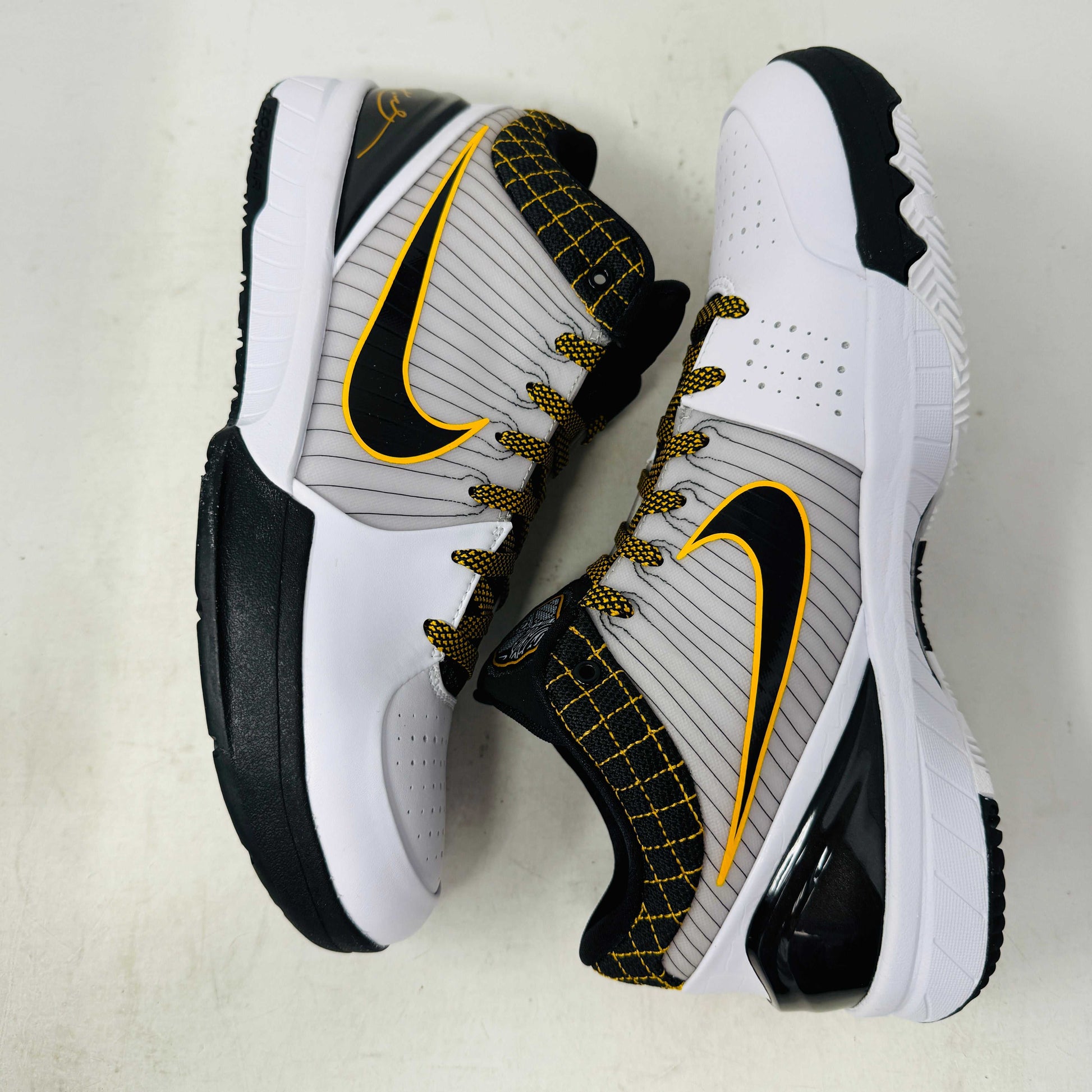 The Nike Kobe 4 Protro White Black Del Sol is a brand-new, authentic Nike sneaker on a shoebox. Predominantly white, it features black and yellow accents with a swoosh logo, a black sole, and yellow-speckled laces, designed for performance and comfort.