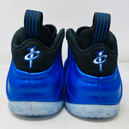 A brand-new Nike Air Foamposite One International Blue sneaker, featuring a striking blue upper with black accents, rests on a sleek black Nike shoebox. It has black mesh laces, a translucent sole with carbon fiber plate, and an iconic side swoosh.