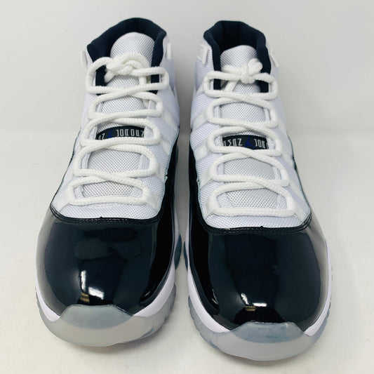 A BRAND NEW black and white Jordan 11 Concord 2018 sneaker sits on its shoebox, showcasing a glossy black patent leather finish and white mesh upper with the iconic Jumpman logo. The shoebox, bearing a white Nike Air logo, ensures these shoes are 100% authentic.