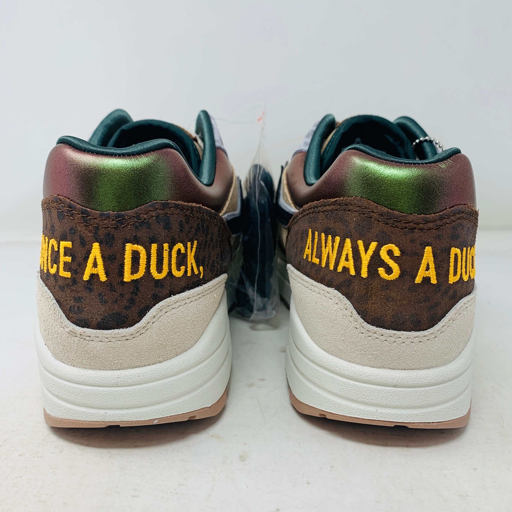 The Nike Air Max 1 87 Premium University of Oregon PE (2024) is a stylish, brand new sneaker featuring a blend of beige, purple, and leopard print with perforated and smooth leather textures. It comes in a vibrant green box and includes a visible air unit in the sole.