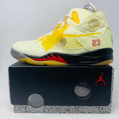 The Jordan 5 Off White Sail sneakers feature a yellow and black design with red accents, a visible air unit, and the number 23 on the side. BRAND NEW in a black shoebox with a red Jumpman logo and speckled base, they include an attached yellow tag and come with EXTRA LACES for versatility.