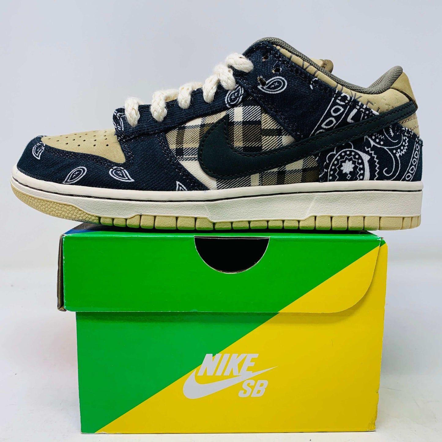 The Nike SB Dunk Low Travis Scott sneakers feature beige suede toe caps, black bandana-patterned overlays, white rope laces, authentic pink accents, and a brown label with text on the tongue. Brand new with extra laces, the interior is visible at the top.