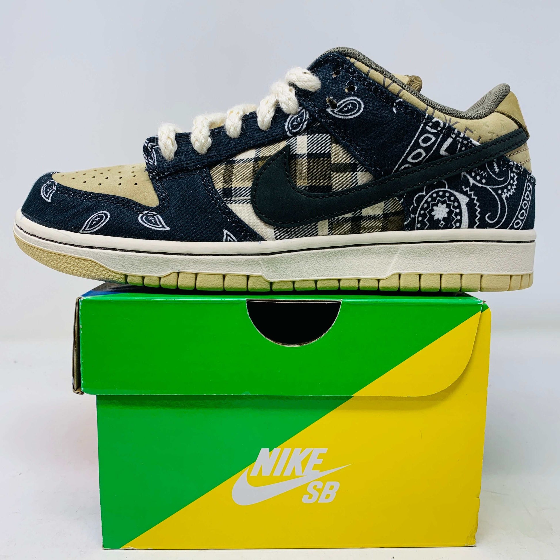 The Nike SB Dunk Low Travis Scott sneakers feature beige suede toe caps, black bandana-patterned overlays, white rope laces, authentic pink accents, and a brown label with text on the tongue. Brand new with extra laces, the interior is visible at the top.