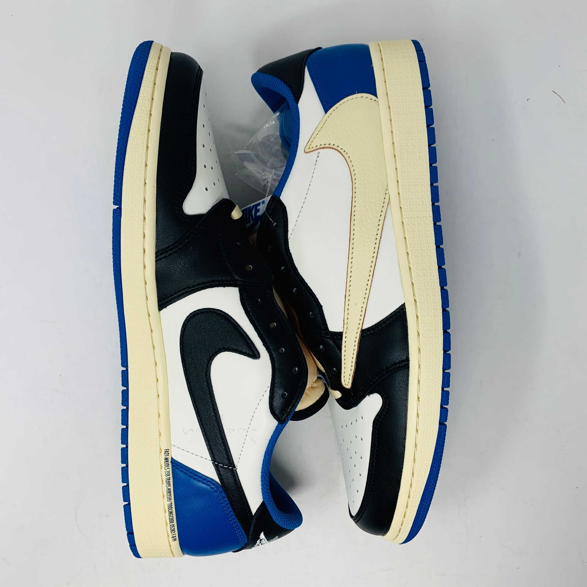 The Jordan 1 Low Travis Scott x Fragment sneakers feature a black and white leather upper with blue accents, a unique beige backward swoosh, and come in a branded Nike box with graphics. These brand-new shoes include an extra set of laces for added versatility.
