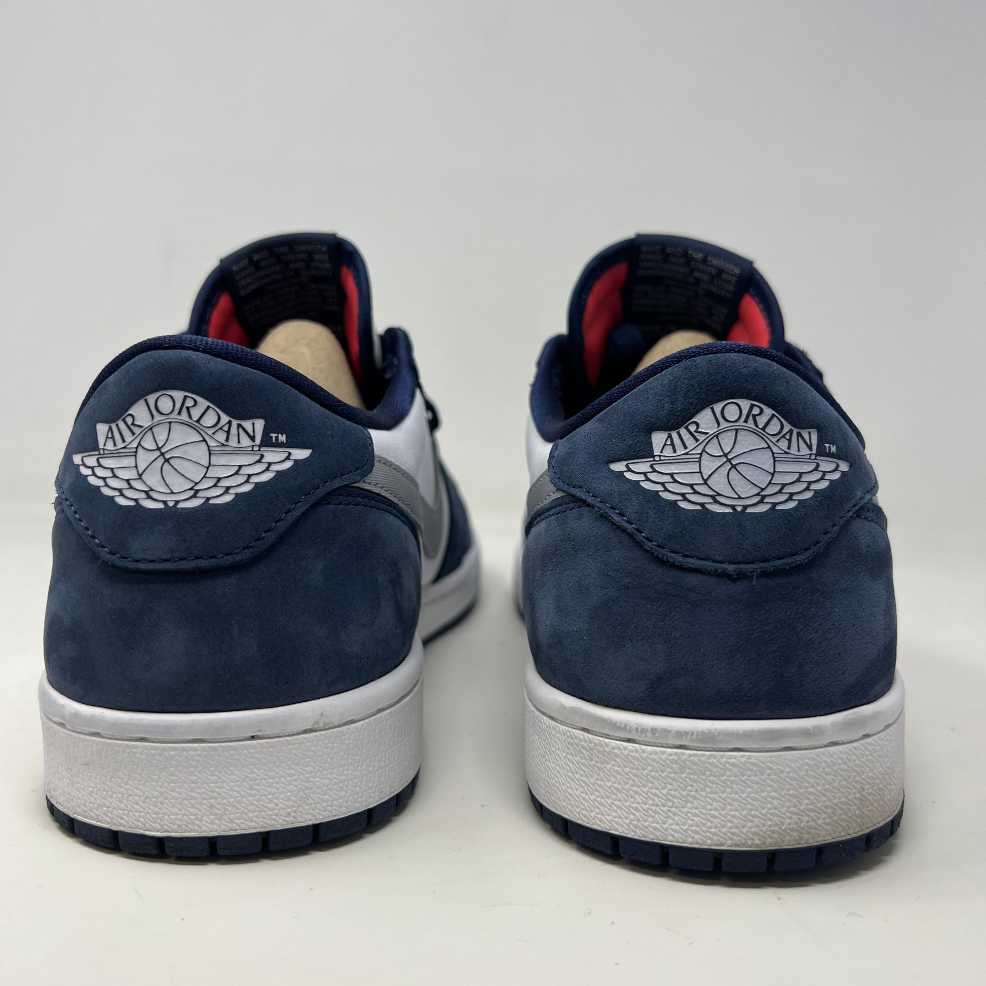 A Jordan 1 Low SB Midnight Navy shoe from Jordan, featuring blue toe and heel, white side panels, and a silver swoosh, is displayed on its box. The VERY CLEAN UPPERS are complemented by the size and product info visible on the label.