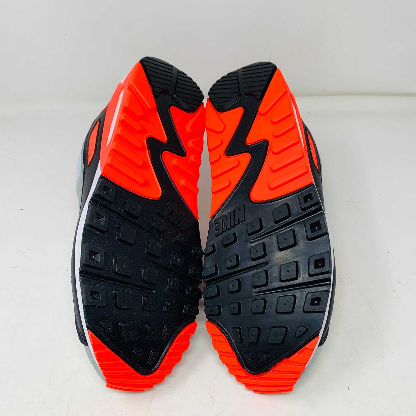 A pair of Nike Air Max 90 Infrared (2020) sneakers in gray, white, and bright orange sits on a pristine shoebox. Beside the shoes are stylish accessories: an orange keychain and spare orange soles.